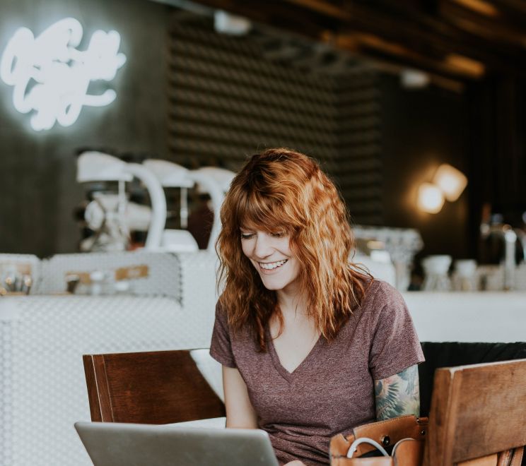 mulher ruiva trabalhando no computador em algo que parece uma cafeteria - trabalhar online com empresa no Brasil